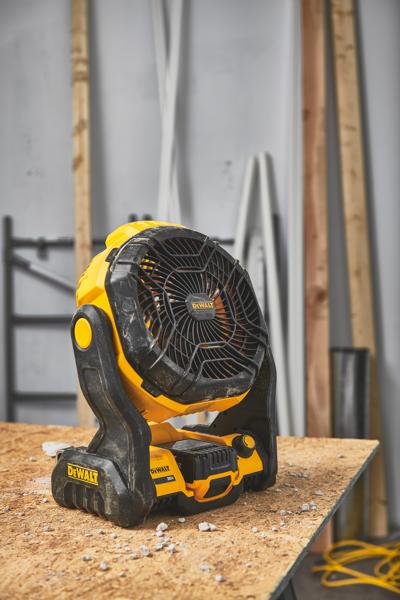 Egy DEWALT hordozható akkumulátoros ventilátor (DCE512B modell) egy fa munkapadon áll egy műhelyben, háttérben építőanyagokkal.